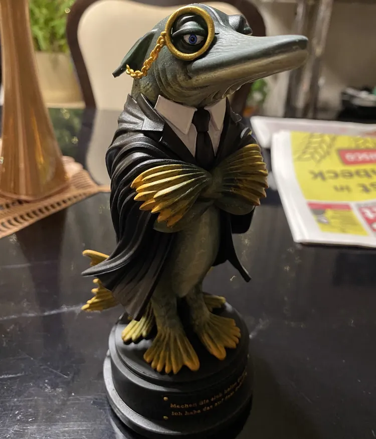 Handgefertigte Kunstfigur &bdquo;Hechtus Advocatus&ldquo;: Hecht im Anwaltstalar mit Monokel, Hemd und Krawatte, auf schwarzem Sockel mit goldener Gravur