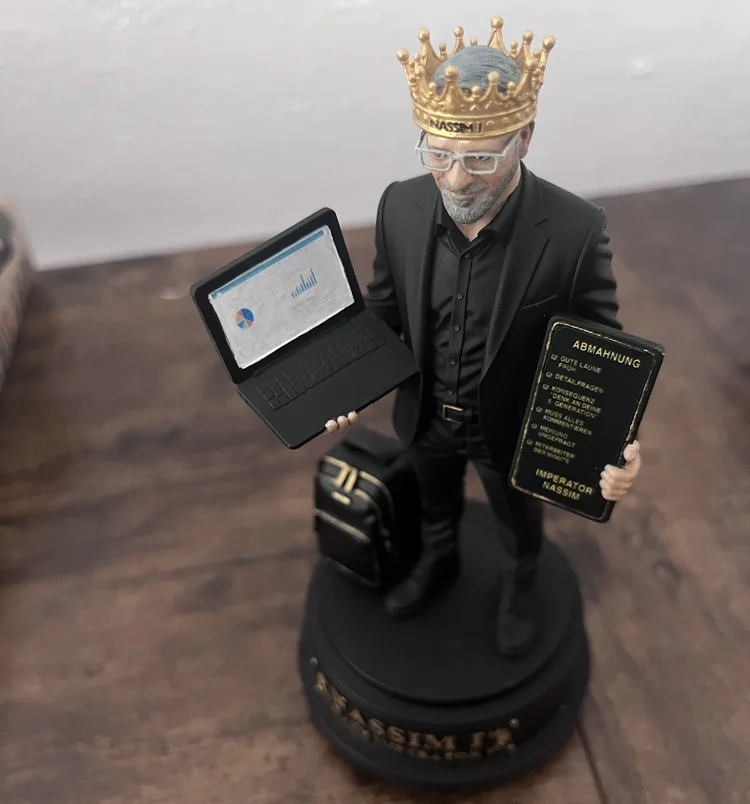 Personalisierte Kunstfigur &bdquo;Imperator Nassim&ldquo;: Mann im schwarzen Anzug mit goldener Krone, Laptop und Tablet in den H&auml;nden, Aktenkoffer daneben, auf schwarzem Sockel mit Goldgravur